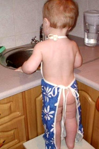 Голопопый малыш, маленький мальчик в фартуке на кухне с голой попой моет посуду, мамин помощник.